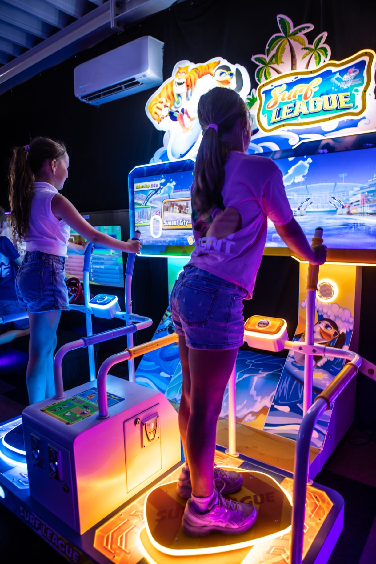 Twee meisjes spelen op de dansmatten terwijl een jongen toekijkt.    
