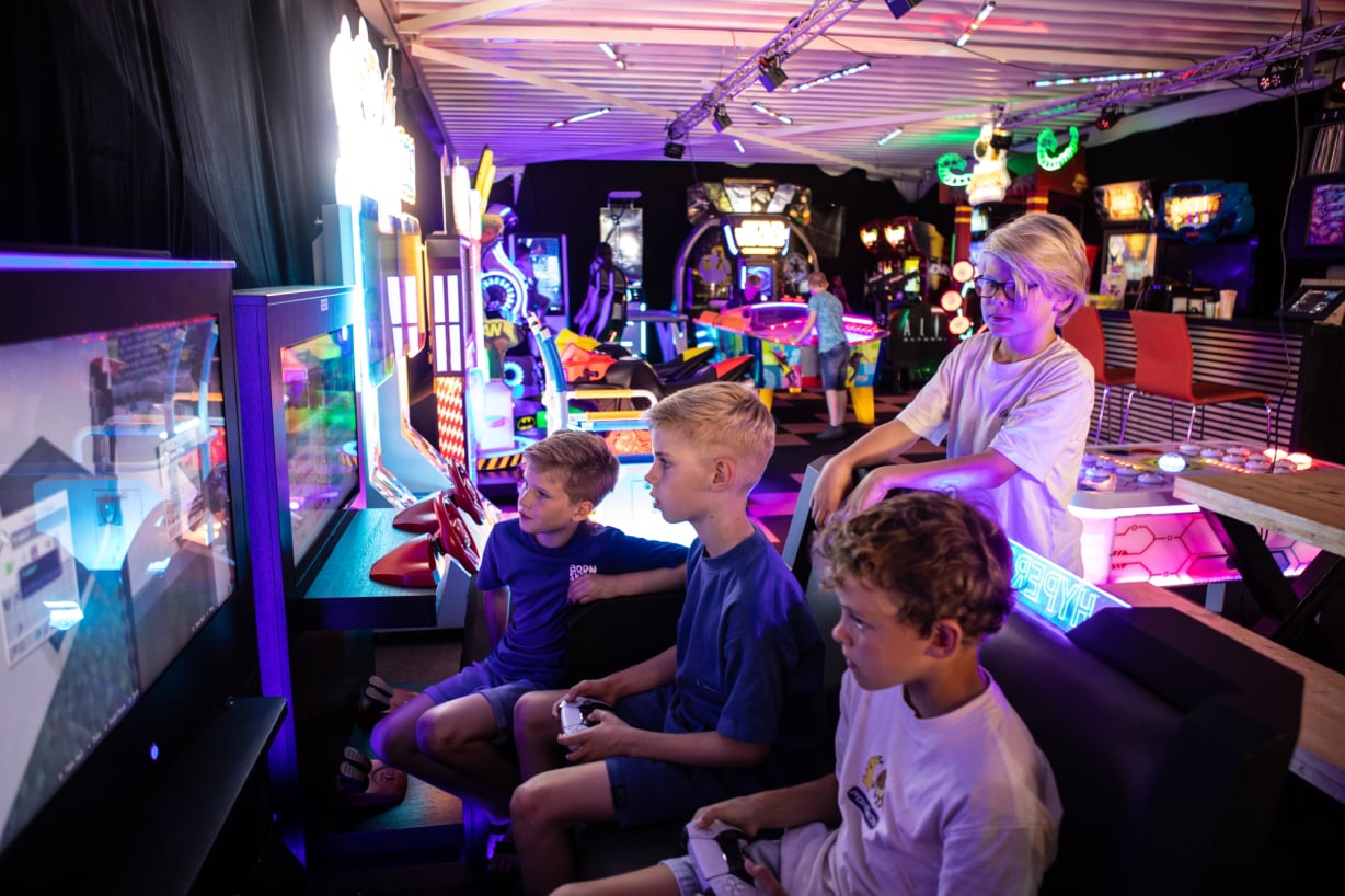 Drie jongens spelen samen op een arcadekast met controllers.  