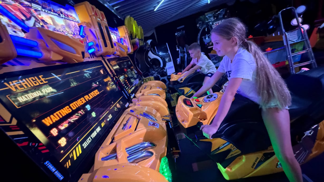 Meisje en jongen kiezen hun motor op de Storm Rider arcadekasten bij Game Lounge Leusden.